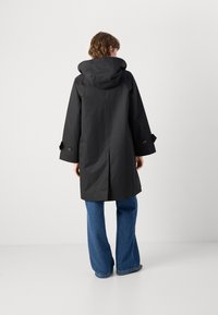 Black waterproof raincoat with a hood, wide sleeves, and large buttons. The back features a straight cut and smooth texture.
