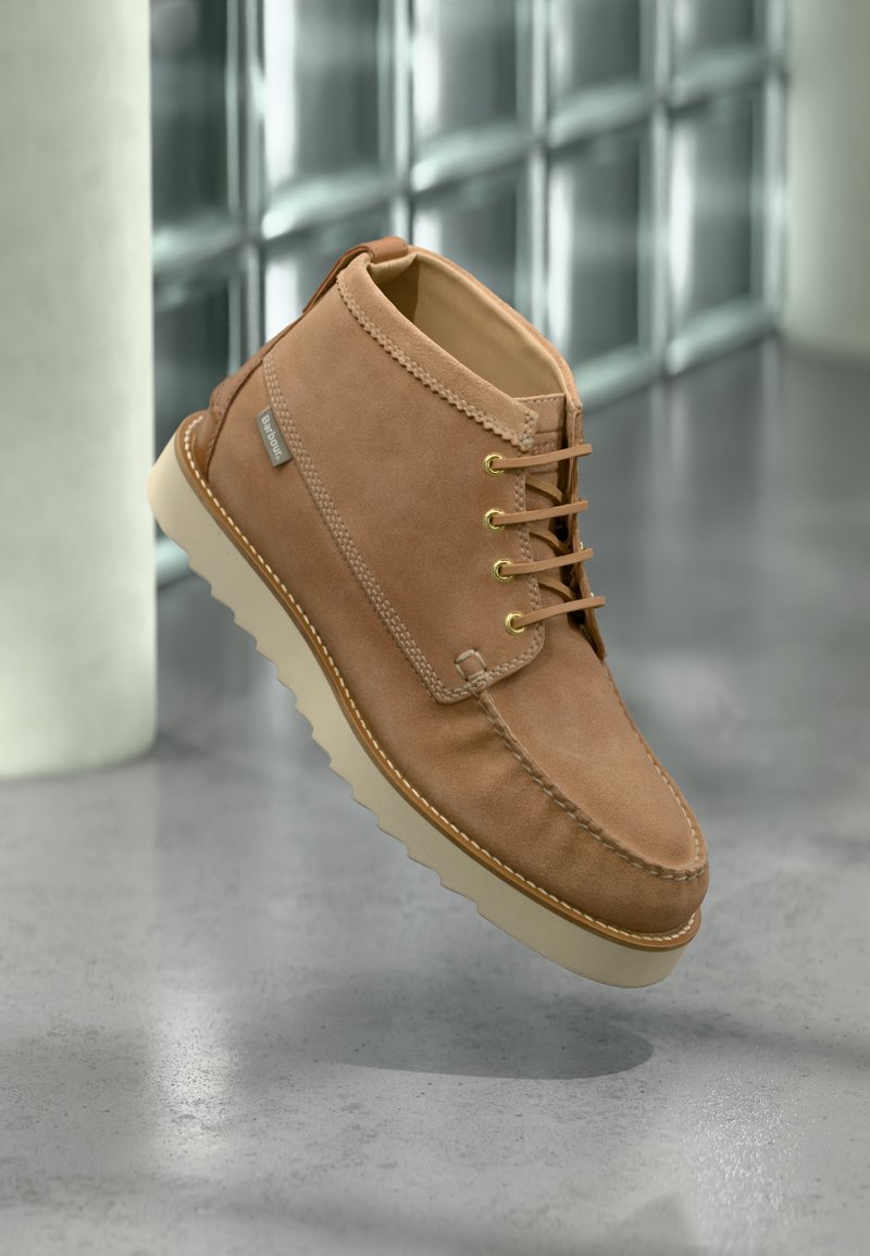 Ταμπά μποτάκι αστραγάλου από σουέντ με μπεζ ραβδωτή σόλα, χρυσά παπούτσια, δερμάτινα κορδόνια και ορατή ετικέτα της μάρκας Barbour στο πλάι.