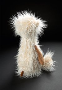 White fluffy plush toy with a shaggy texture, brown suede accents on ears and tail, and a rounded shape. Positioned upright against a dark background.