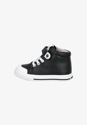Zapatilla alta de cuero negro con puntera y suela de goma blanca, con cordones y una banda de Velcro, acentuada por un logotipo circular en la banda.