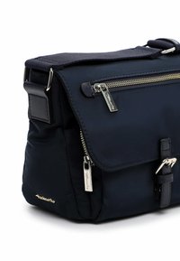 Granatowa nylonowa torba na ramię z metalowymi elementami, kieszeniami na zamek i zapięciem na klamrę. Miękka w dotyku o usztywnionej konstrukcji.