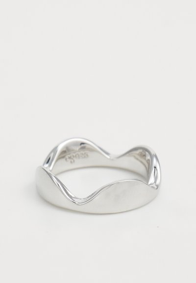 Anello di argento liscio con un design ondulato, finitura lucida e incisione del marchio sulla banda interna, impostato su uno sfondo bianco semplice.