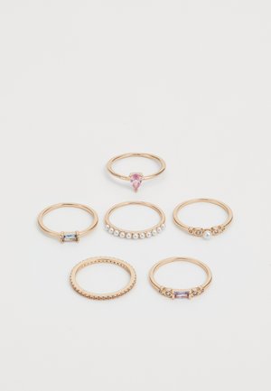 Set of seven gold-tone rings featuring varied designs: one with a pink stone, one with pearls, and others with colored accents and patterns.