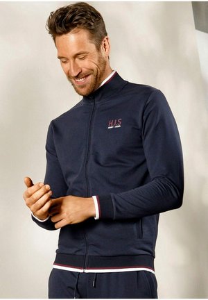 Marineblaue Zip-Jacke aus weichem Baumwoll-Mix, mit weißen und maronenfarbenen Akzenten an den Bündchen und am Saum, sowie einem kleinen Logo auf der Brust.