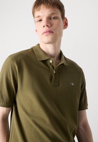 Oliven grøn polo-shirt med klassisk krave, to-knap lukning og tekstureret stof med en lille logo detalje på brystet.