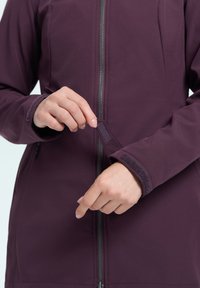 Giacca viola da donna con zip frontale, polsini aderenti e dettagli in Velcro, che mette in evidenza un tessuto liscio e texturizzato.