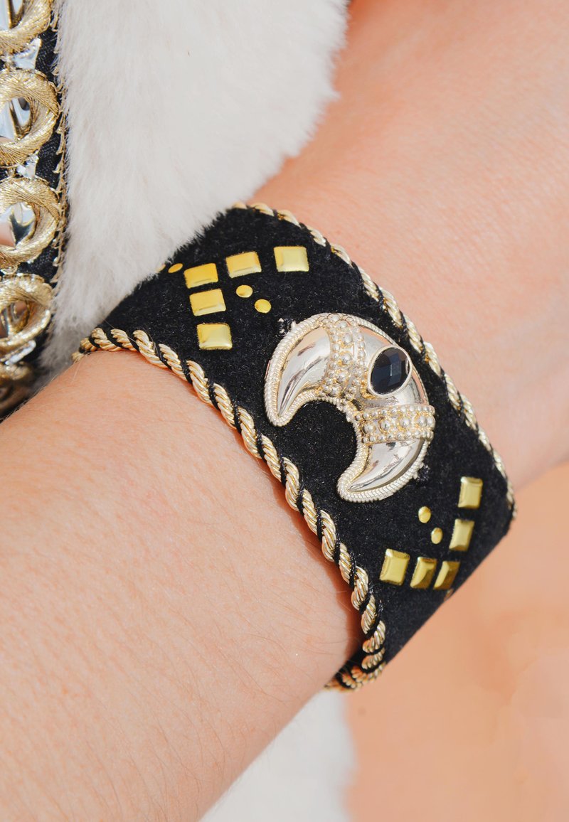 Poignet en cuir suédé noir orné d'accents carrés jaunes, de bordure tordue dorée et d'un détail décoratif en argent en forme de griffe avec une pierre noire.