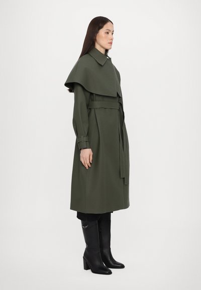 Πράσινο μάλλινο παλτό με φαρδύ γιακά, ζώνη στη μέση και μακριά μανίκια, σε συνδυασμό με μαύρες μπότες μέχρι το γόνατο που έχουν ασημένια λεπτομέρεια.