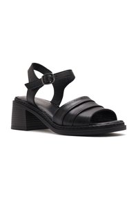 Black leather heeled sandals with cross straps, an open toe design, and buckle closure. Moderate block heel with textured sole.