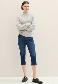 Vaaleanharmaa ribbineulottu korkeakauluksinen neule, yhdistetty tummansinisiin polvipituisisiin farkkuihin ja mustiin nauhallisiin kenkiin. Yksinkertainen muotoilu, istuva malli.