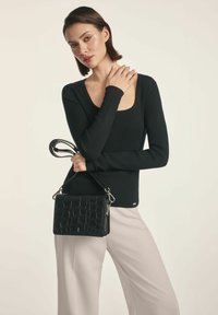 Czarna torebka ze tłoczeniem w krokodyla z odpinanym paskiem, zestawiona z dopasowanym czarnym swetrem w prążki i jasnymi spodniami.