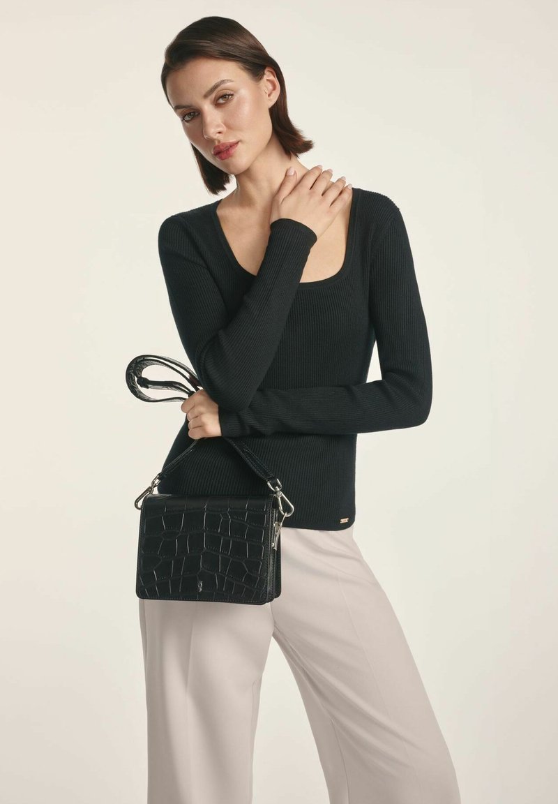 Czarna torebka ze tłoczeniem w krokodyla z odpinanym paskiem, zestawiona z dopasowanym czarnym swetrem w prążki i jasnymi spodniami.