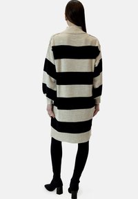 Abito in maglia color beige e nero a righe, con collo a imbuto, maniche lunghe e polsini e orlo a coste. La lunghezza arriva a metà coscia.