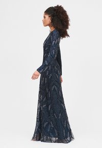 Marineblaues, langärmliges Kleid mit filigraner silberner Blattstickerei, verziert mit Perlen und einem fließenden Schnitt. Strukturierter Spitzenstoff.