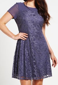 Robe en dentelle violette à manches courtes, mettant en avant un motif floral texturé, un corsage uni et une jupe évasée s'étendant au-dessus du genou.