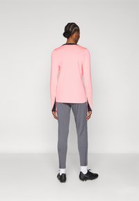 Top roz deschis cu mânecă lungă și accente negre, asociat cu pantaloni gri tapered. Materialul pare neted, cu un design ajustat și fermoare la glezne.