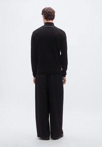 Svart poloskjorte med lange ermer, flat krage og hvit detalj, kombinert med løstsittende svarte bukser. Jevn tekstur og ensfarget.