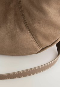 Borsa a mano in suede marrone, texture morbida, forma arrotondata e ampia tracolla in pelle con dettagli di cucitura a contrasto.