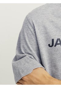 Camiseta de algodón gris con mangas cortas enrolladas y la palabra "JANE" en letras negras en negrita en el frente.