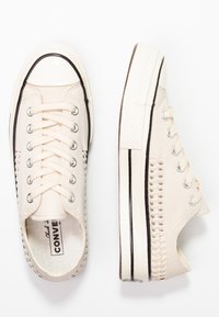 Baskets en toile beige avec accents en caoutchouc noir, coutures latérales texturées et bout rond. Dotées d'œillets métalliques et de lacets plats.