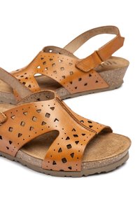Sandalias de cuero marrón con patrones geométricos cortados, plantilla de corcho, correa ajustable y suela de cuña. Superficie texturada para mayor comodidad y agarre.