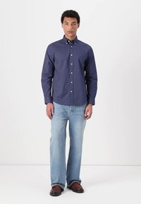 Marineblauw knoopshirt met witte stippen, lange mouwen en een kraag; gecombineerd met lichtblauwe spijkerbroeken en bruine schoenen. Eenvoudig ontwerp.