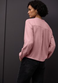 Blusa rosa a maniche lunghe con scollo arricciato, texture liscia e piega sul retro, abbinata a jeans neri. Design semplice ed elegante.