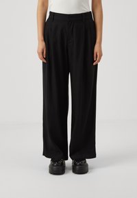 Svarta vida byxor med framfåror, tillverkade av lättviktsmaterial. Har en skräddarsydd midja och matchas med kraftiga svarta plattformsskor.