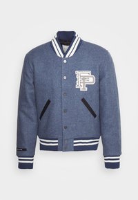 Blå ull varsityjacka med vitrandiga ribbade kragar och muddar, frontknäppning, två sidofickor och en patchlogotyp på bröstet.