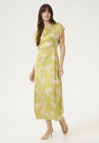 Maxi šaty v světle růžové barvě s vzorem zelených listů, krátké rukávy typu cap, detail na boku s uzlem a splývavý materiál. Hladká textura, délka nad kotníky.