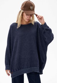 Oversized granatowy sweter z teksturowanym splotem, szerokimi rękawami i ściągaczem. Połączony z brązową czapką z detalem serca w panterkę.