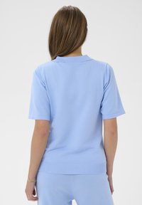 Polo bleu clair à manches courtes en maille douce et texturée. Dispose d'un col et d'un ourlet côtelés, conçu pour une coupe décontractée.