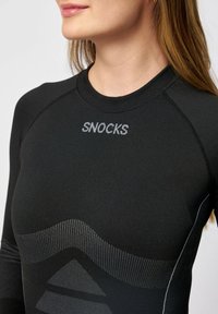 Svart långärmad performance-top med texturerade mönster och reflekterande "SNOCKS"-logotyp. Har en figurnära design och kontrasterande sömmar.
