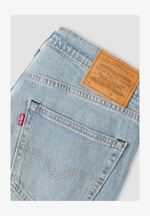 Lichtblauwe spijkerbroek van denim, opgevouwen om het achtervak en het bruine leren Levi Strauss & Co.-label met een rood Levi's-label op de naad van het zakje te tonen.