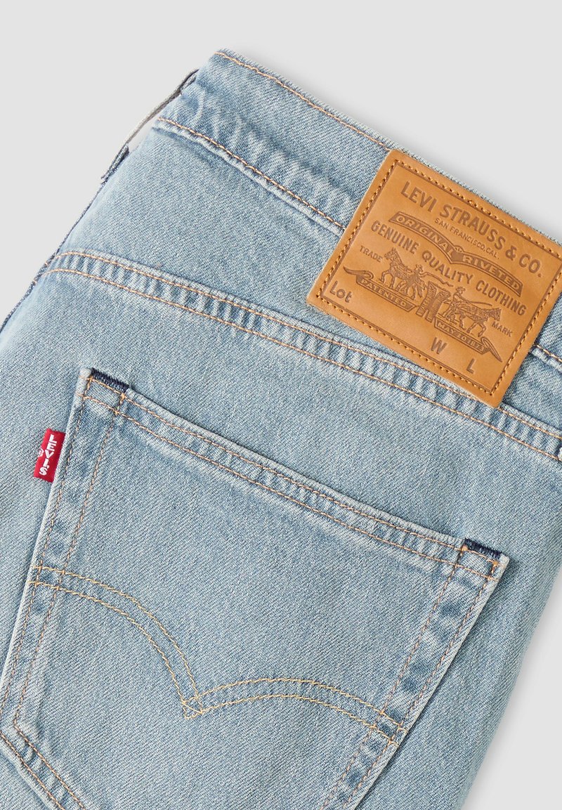 Jean en denim bleu clair plié pour montrer la poche arrière et le patch en cuir marron de Levi Strauss & Co. avec l'étiquette rouge Levi's sur la couture de la poche.