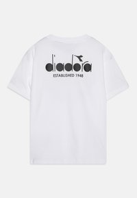 Valkoinen puuvillapaita, jossa on musta logo "diadora" ja tekstillä "ESTABLISHED 1948" painatus takana. Lyhyet hihat ja normaali istuvuus.