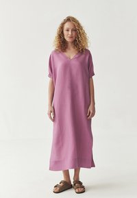 Lang, let passet kjole i blødt pink stof med V-udskæring og korte puffærmer. Har lige søm og sideslids. Kombinationen med brune sandaler.