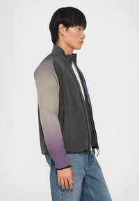 Fleece striukė su aukštu apykakle, pilkos spalvos, pereinančios į purpurinę rankovėse, su užtrauktuku užsegama kišene ir prigludusiomis apykaklėmis.