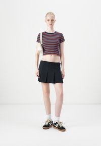 Raidallinen crop-top lyhyillä hihoilla, musta laskostettu mini-hame, valkoiset tennarit mustilla yksityiskohdilla ja pieni valkoinen laukku.