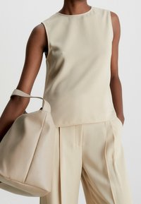 Beige ärmlös topp med en mjuk textur, kombinerad med matchande byxor och en stor, mjuk väska över armen.