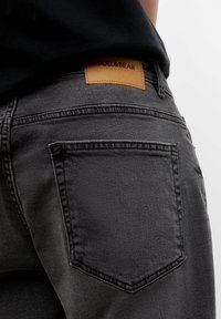 Jeans de mezclilla gris con un parche de cuero de Pull&Bear, que presentan bolsillos traseros estándar y detalles de costura visibles.