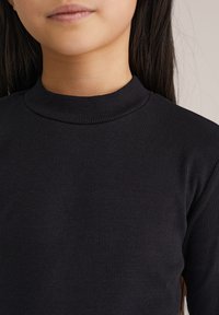 Top negro de manga larga con ribetes, cuello alto, tejido texturizado y ajuste ceñido alrededor del cuello y los hombros.