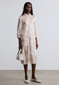 Φόρεμα ανοιχτού ροζ χρώματος με ανθισμένο μοτίβο, γιακά και μανίκια 3/4, κατασκευασμένο από μαλακό ύφασμα. Συνδυάζεται με λευκή τσάντα χειρός και μπεζ μπαλαρίνες.