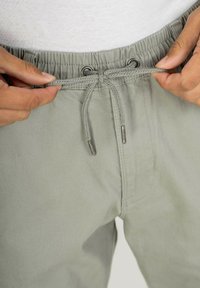 Helle graue Shorts mit einem elastischen Bund, einem Kordelzug mit Metallenden und seitlichen Taschen, ausgestattet mit einer glatten Stofftextur.