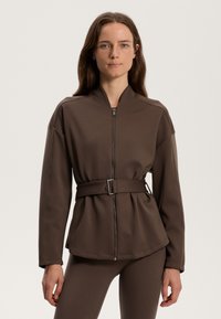 Brun zip-up jacka med hög krage, bälte i midjan och långa ärmar, tillverkad av ett mjukt, stretchigt material. Designad för en skräddarsydd passform.