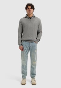 Grijs geribbelde pullover met half-zip kraag, gecombineerd met lichtblauwe versleten denim jeans en beige veterschoenen.