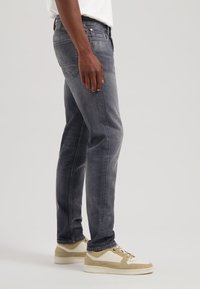 Jeans din denim gri cu o croială slim, având decolorări subtile și un design clasic cu cinci buzunare, asortați cu adidași bej și albi.
