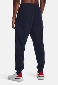 Pantalones deportivos azul marino con un corte ajustado, que cuentan con una cinturilla elástica, bolsillos laterales y un bolsillo trasero. Llevados con zapatillas blancas y rojas.