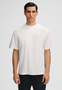 Witte katoenen t-shirt met korte mouwen, ronde halslijn en een relaxte pasvorm. Heeft een zijlabel en een gladde textuur. Gecombineerd met donkere jeans.