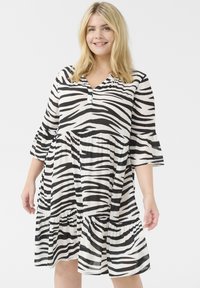 Schwarzes und weißes Kleid mit Zebra-Muster, V-Ausschnitt, weit geschnittenen Dreiviertelärmeln und gestuftem Saum. Hergestellt aus leichtem Material.